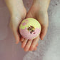 A person holding a colorful bath bomb with a pink, yellow, and green exterior, 