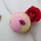 A pink bath bomb with rose petals on a marble surface.