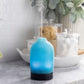 A blue essential oil diffuser with a sea glass effect, placed on a kitchen countertop, emitting a vapor.