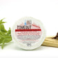 A shower steam tablet with the label 'TIMEOUT' Immortal, placed on a wooden piece next to green leaves, intended to enhance shower experience with essential oils.