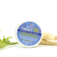 A shower steam tablet with packaging, labeled 'Time Out Who's Vick', with a wooden stick and green leaves in the background.