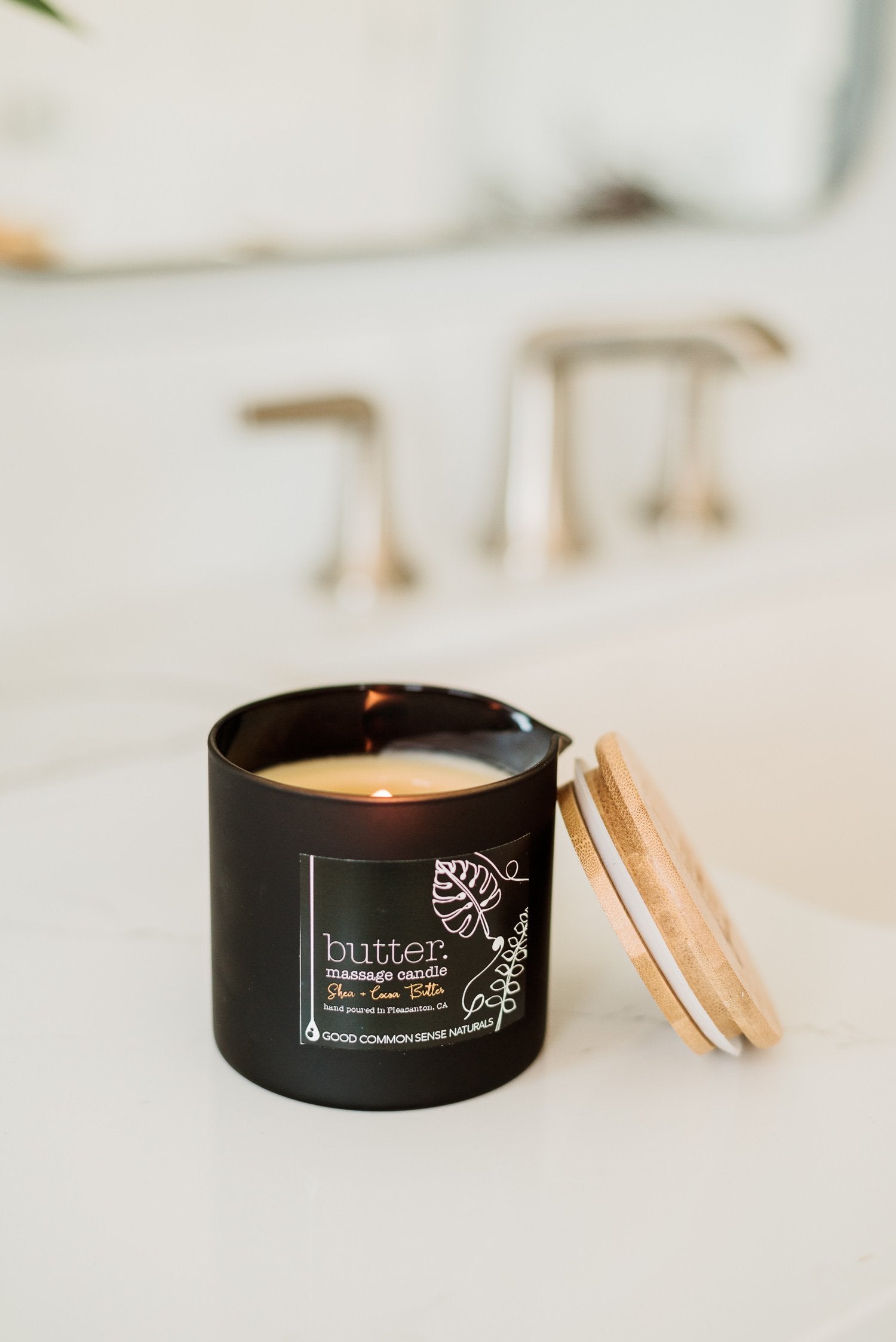 candle in a black container with a pour spout lit in a bathroom setting 