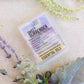 sweet surrender wax melt see through container. with plants surrounding on tan backround 