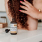 brown dropper bottle labeled Argan Rescue, Hair Serum, on white counter 