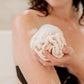A person holding a white cotton crochet loofah in a bathroom setting.