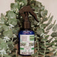 A spray bottle labeled 'CRAP TRAP Spray' with a blue liquid, placed on a surface with green foliage in the background.
