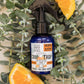 A spray bottle labeled 'Orange You Crappy, Toilet Spray' with an orange slice and green foliage in the background.