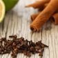 A collection of essential oils including clove, orange, frankincense, lemon, and cinnamon, presented in a shattered blend on a white surface with a slice of lemon and cinnamon sticks in the background.
