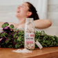glass jar filled with pink bath salts with flowers in background 