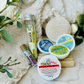 Therapeutic Waters, Gift Set including Four Shower Steam Tabs, Facial Disk, Herbivore Bath Salt tube, and Lip balm. all laying on a towel and on counter. 